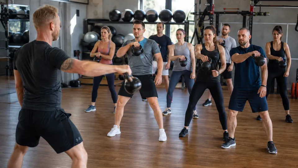 Zajęcia grupowe w sali fitness klubu, uczestnicy w średnim wieku ćwiczą z instruktorem